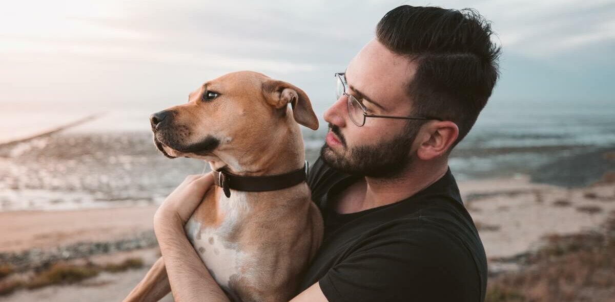 Homem segura cachorro no colo em uma praia
